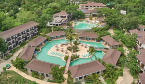 Aerial view of a luxury tropical resort featuring circular lagoon-style swimming pools surrounded by private villas and lush green forest.